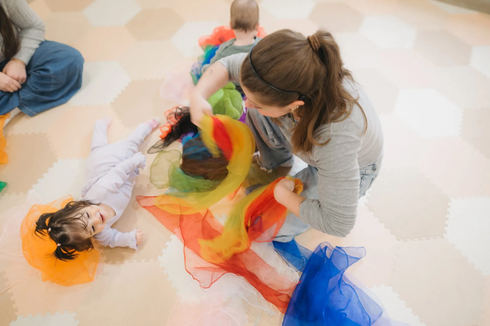 Babies playing with rainbow scarves on the floor at Rockin' with Rach sensory music class Toronto