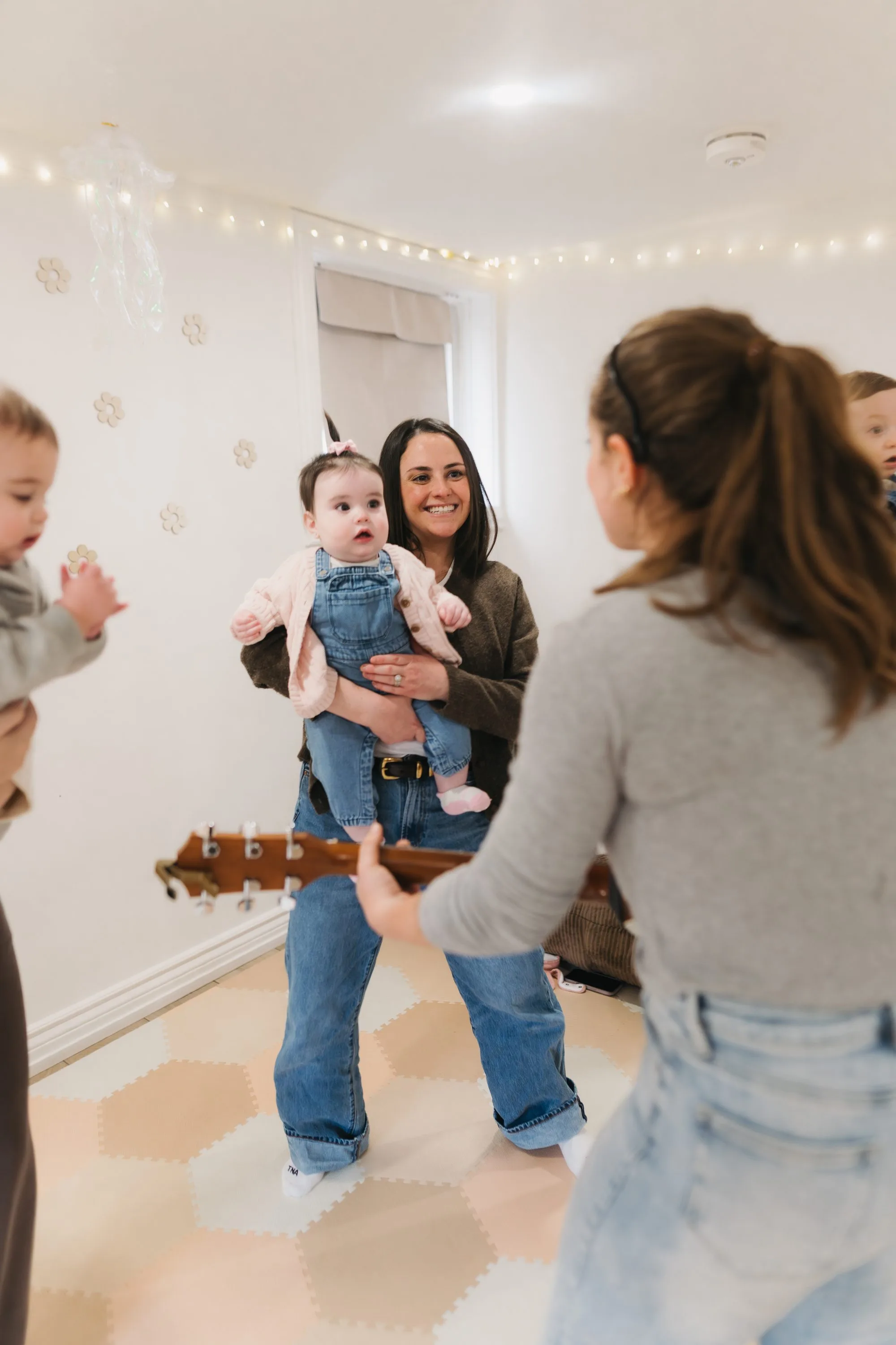 Mom lifting baby girl in denim overalls at Rockin' with Rach baby music class Toronto