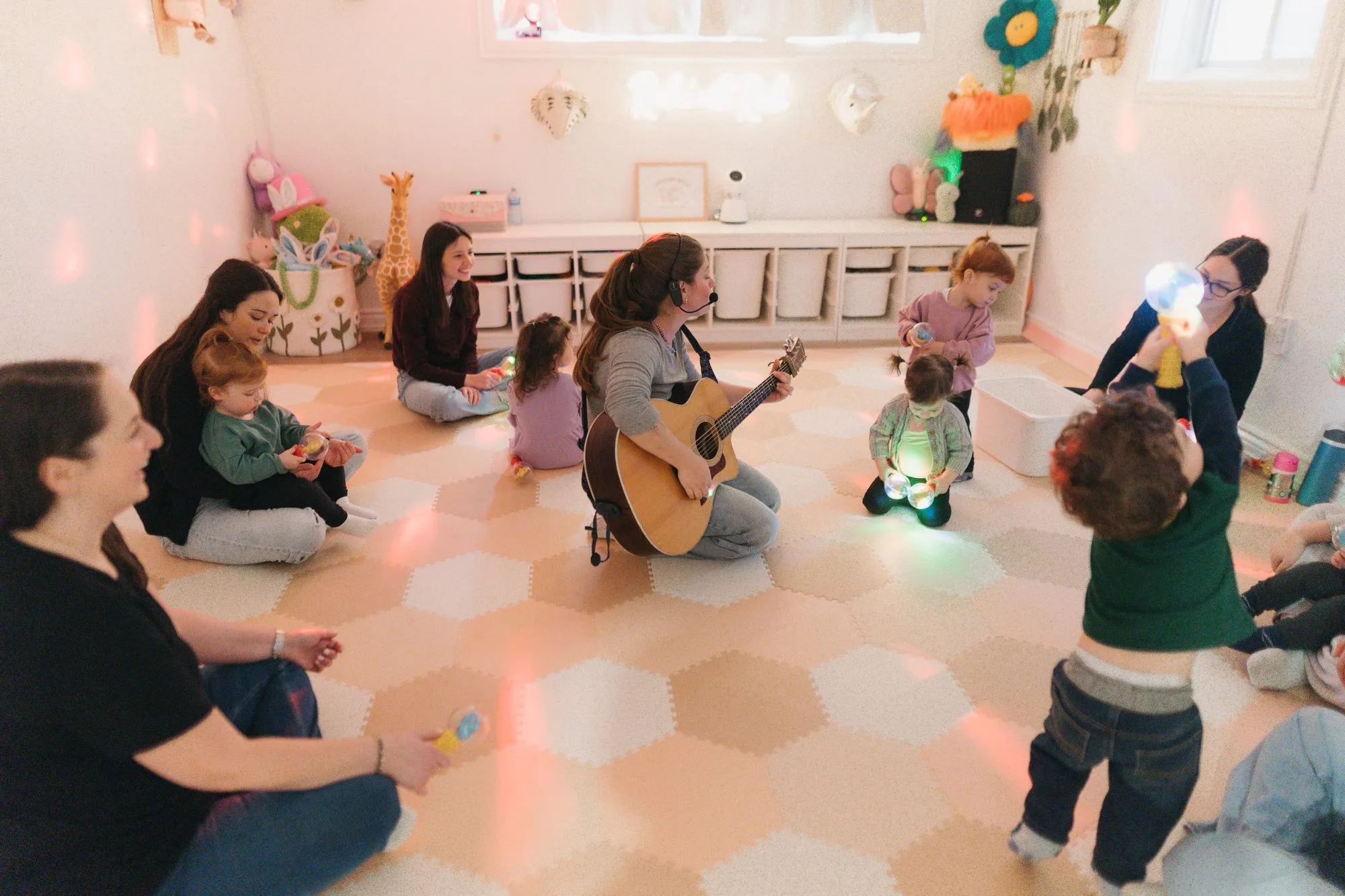 Rachel playing guitar for a circle of babies and caregivers during light show at Rockin' with Rach Toronto