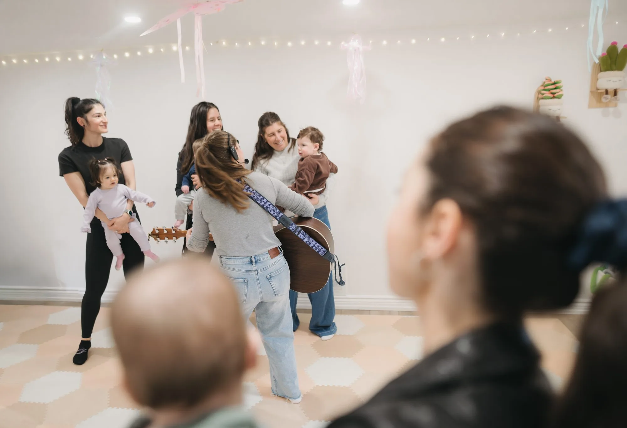 Rachel playing guitar for a circle of babies and caregivers with streamers at Rockin' with Rach Toronto
