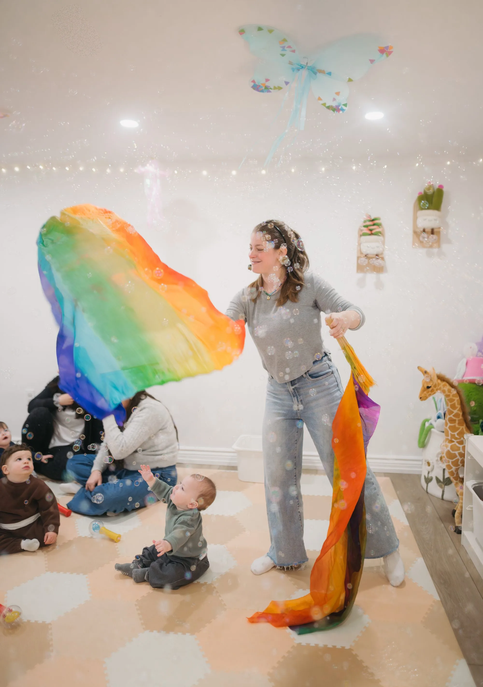 Rachel waving rainbow scarf as a baby reaches out at Rockin' with Rach Toronto
