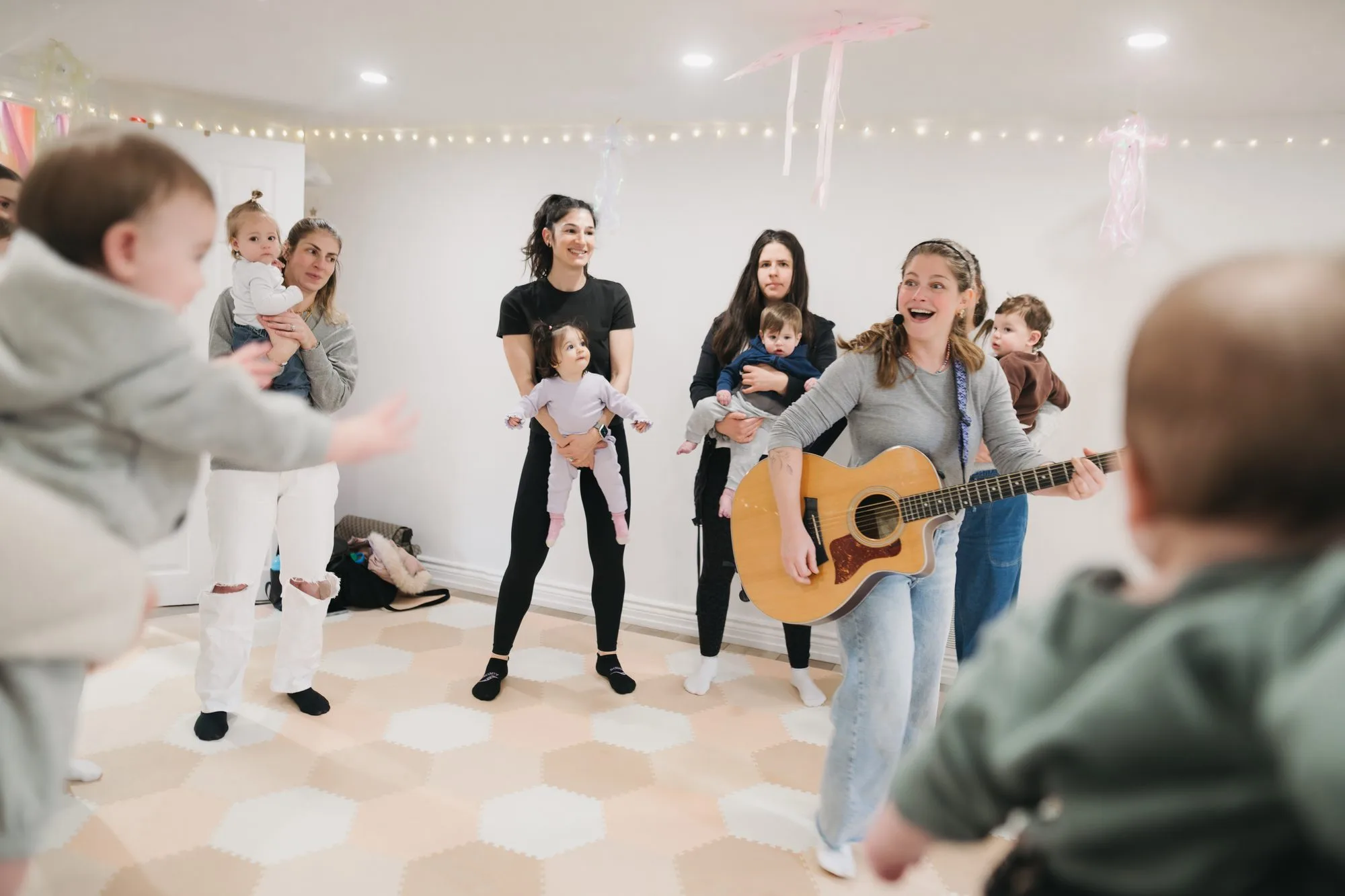 Rachel singing and playing guitar for moms and babies with pink streamers at Rockin' with Rach Toronto