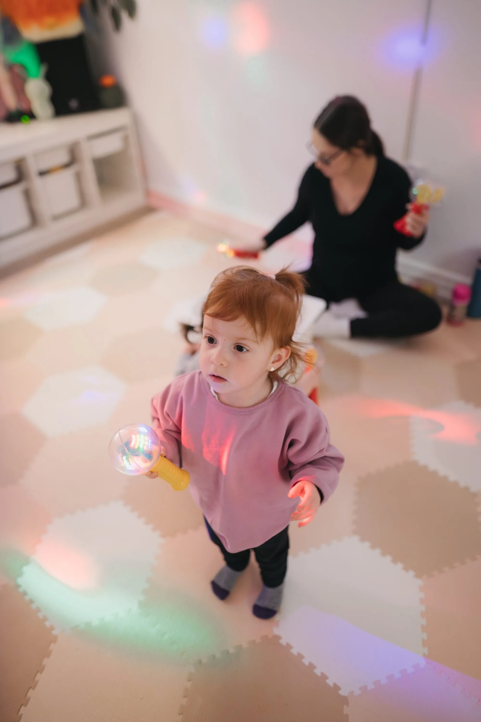 Toddler girl standing and waving a light wand at Rockin' with Rach music class Toronto