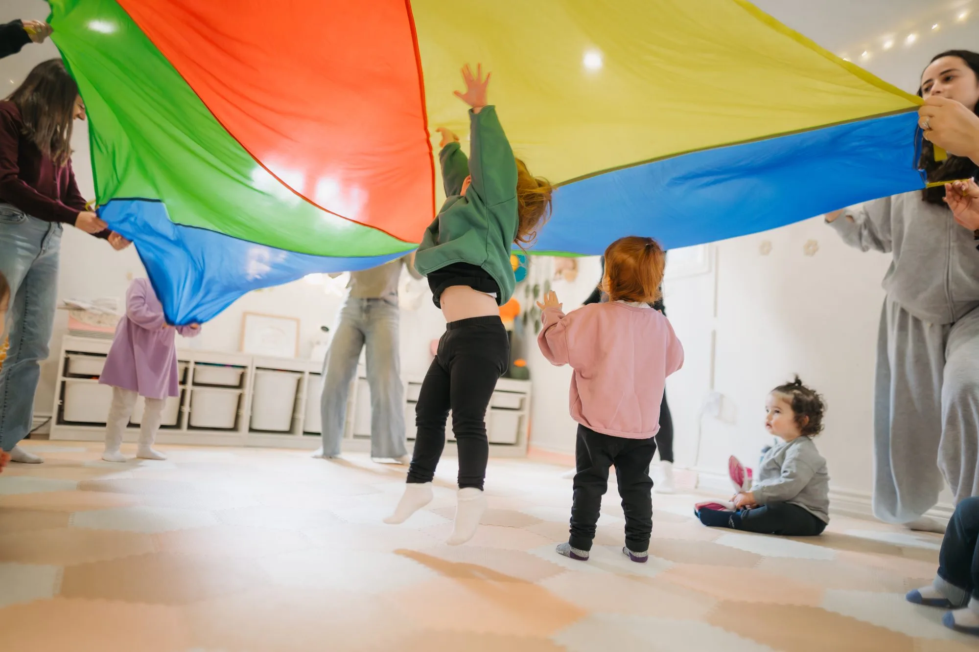 Toddlers jumping under a rainbow parachute at a Rockin' with Rach special event in Toronto