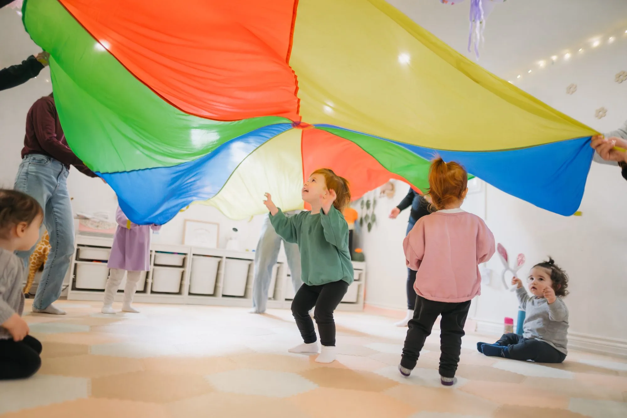 Toddlers playing under a colourful rainbow parachute at Rockin' with Rach studio Toronto
